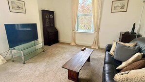 Una sala de estar con un mueble de televisión de vidrio, una mesa de centro de madera, un sofá de cuero y un armario oscuro.
