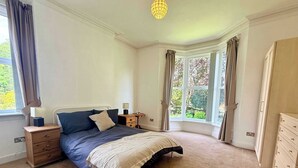 A bedroom with a bed, nightstands, a dresser, and a window with curtains.