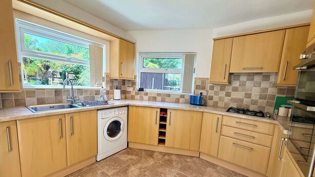 A kitchen with wooden cabinets, a washing machine, a sink, and a window with a view of greenery.