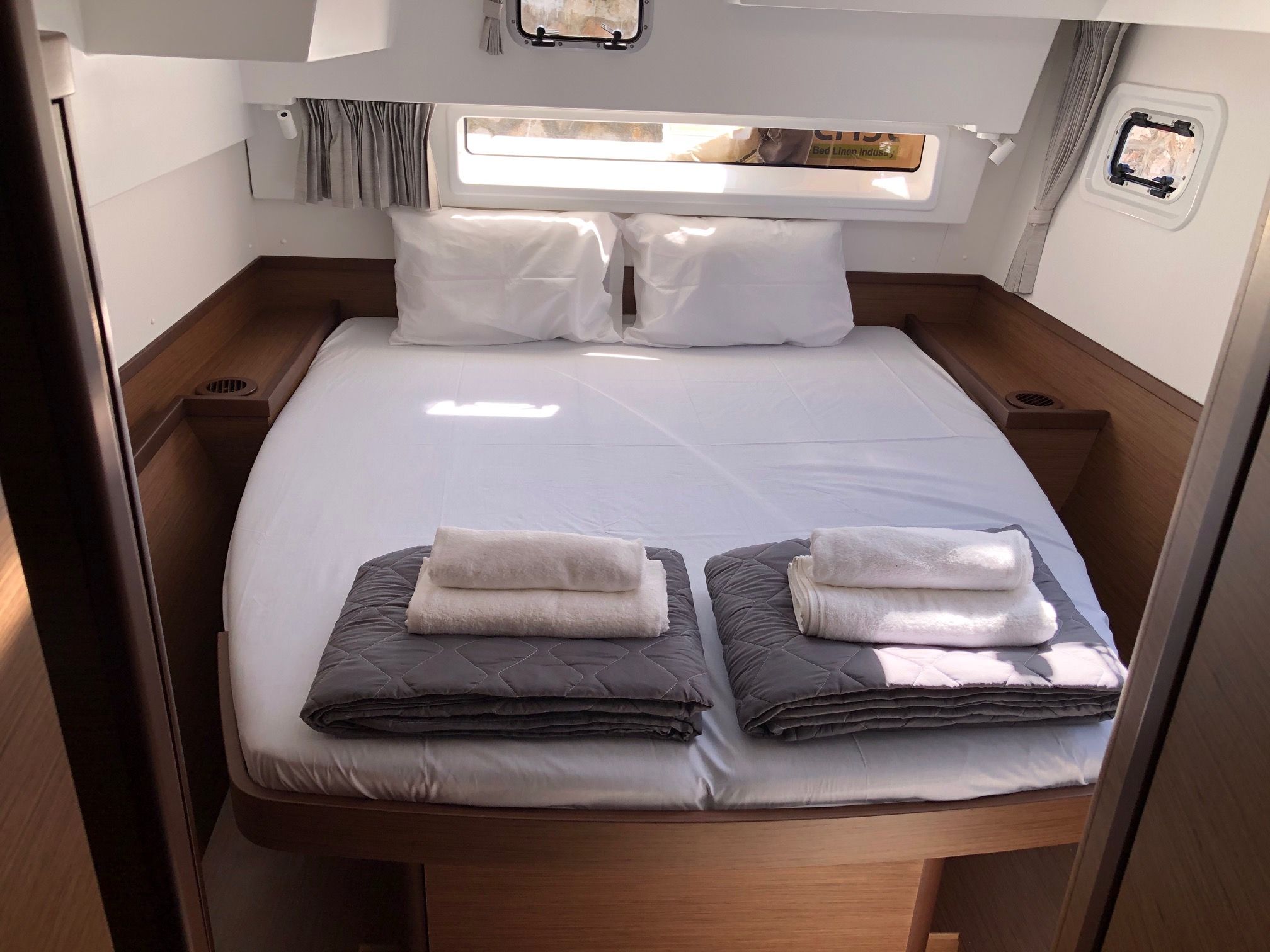 Una cama bien hecha con almohadas, una ventana con cortinas y un estante con una revista.