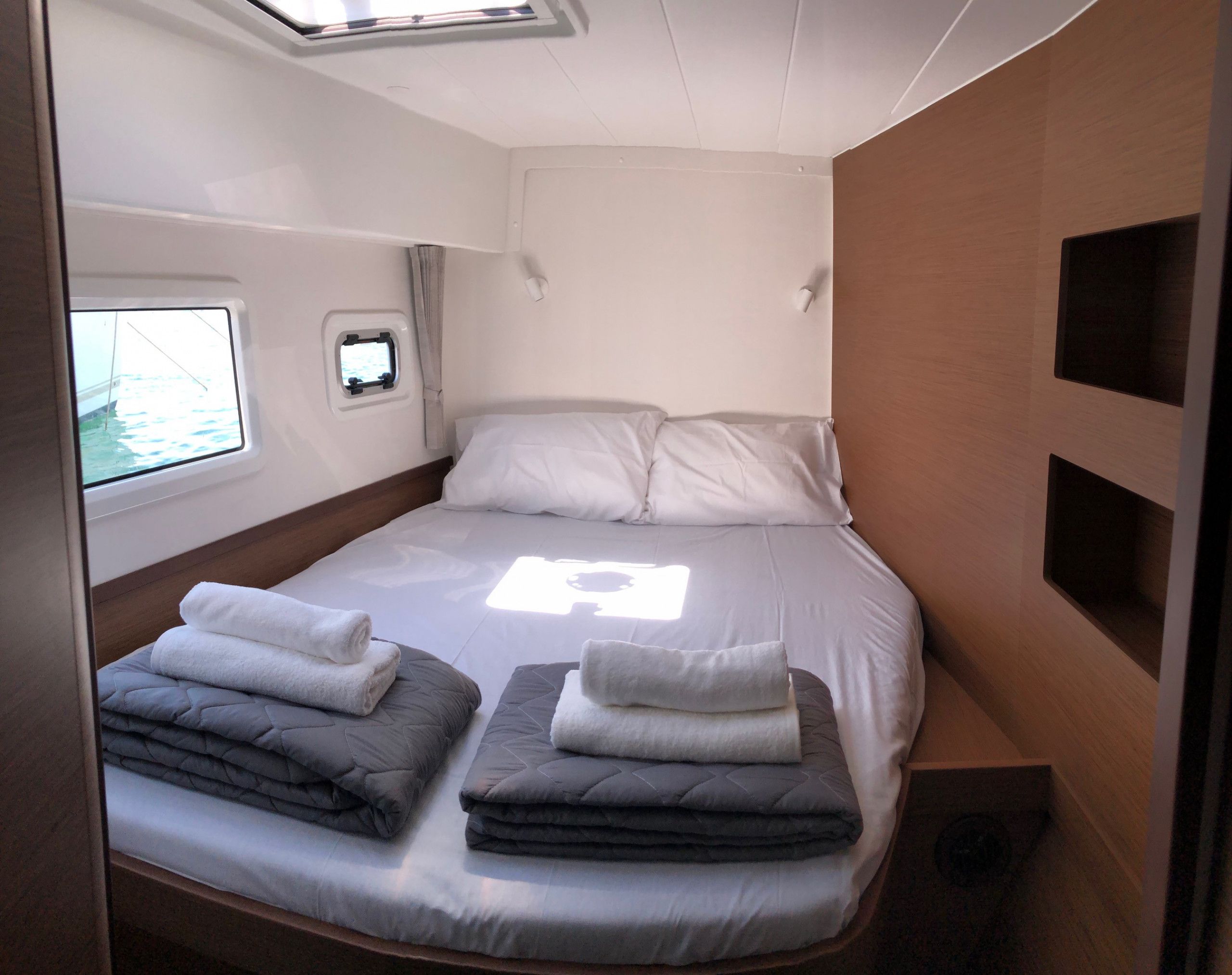 Une petite chambre comprenant un lit, deux oreillers, une fenêtre et un petit téléviseur.