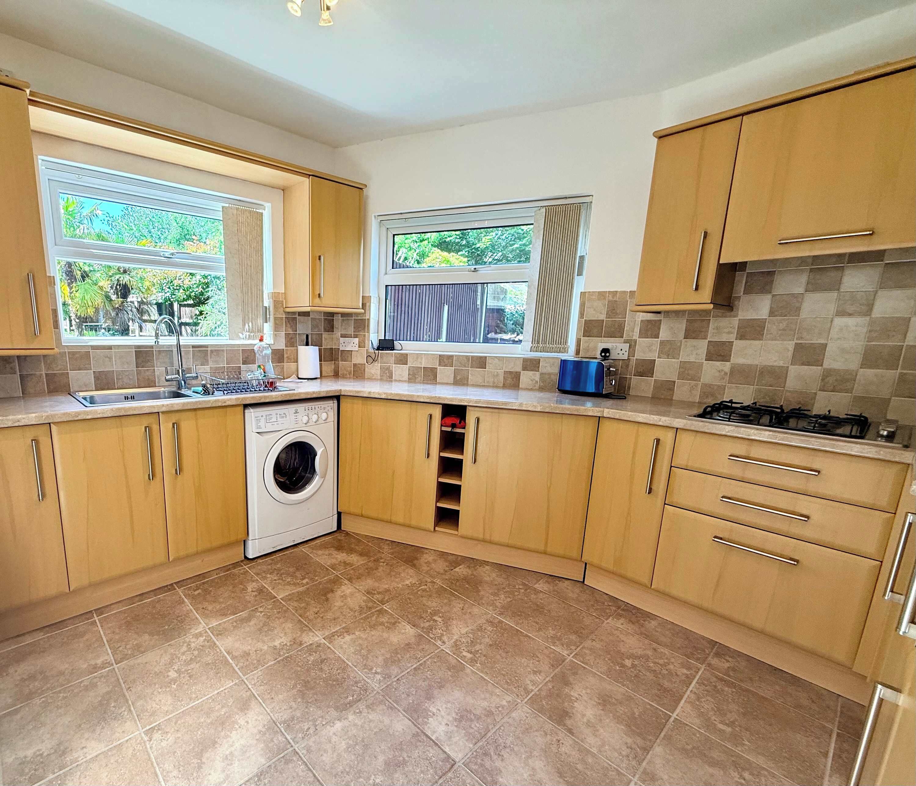 A kitchen with wooden cabinets, a washing machine, a stove, and a window with a view of greenery.