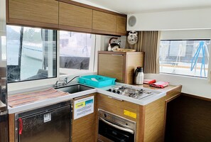 A compact kitchen with a sink, stove, and oven, wooden cabinets, and a window with a view of boats. - Sun-Kissed Sailing Adventure in Isla de Mahe, Seychelles (Providence)