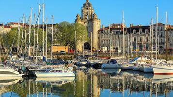 Un port de plaisance où sont amarrés de nombreux bateaux, un bâtiment historique imposant en arrière-plan et un ciel bleu dégagé.