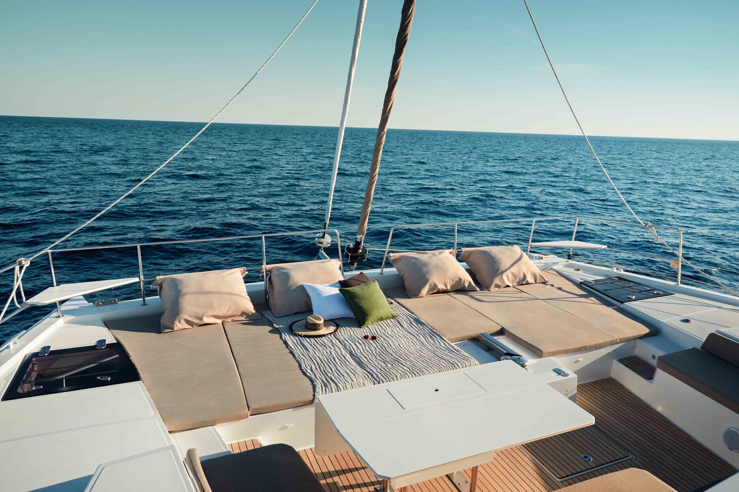 A sailboat deck with cushioned seating, a table, and a view of the open sea.
