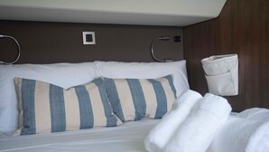 A neatly made bed with striped pillows, a white blanket, and a rolled towel. - Sun-Kissed Sailing Adventure in Islas Baleares, Mallorca (Andratx)