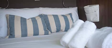 Un letto ben rifatto con cuscini a righe, una coperta bianca e un asciugamano arrotolato.