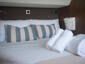 Ein ordentlich gemachtes Bett mit gestreifter Bettwäsche, einem weißen Überwurf und einem aufgerollten Handtuch.