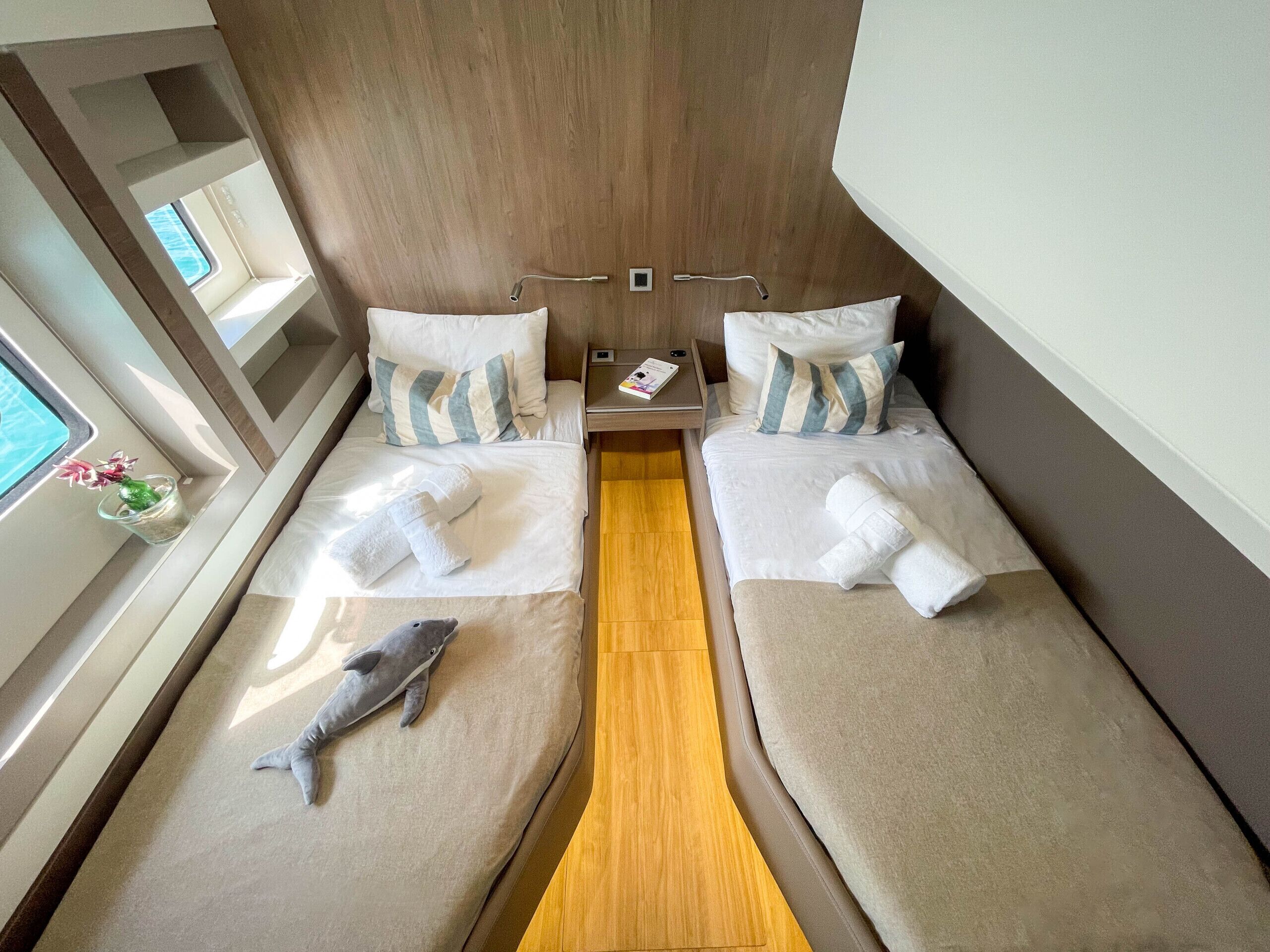 A cabin with two beds, a wooden panel wall, a small table with a book, and a window with a view.