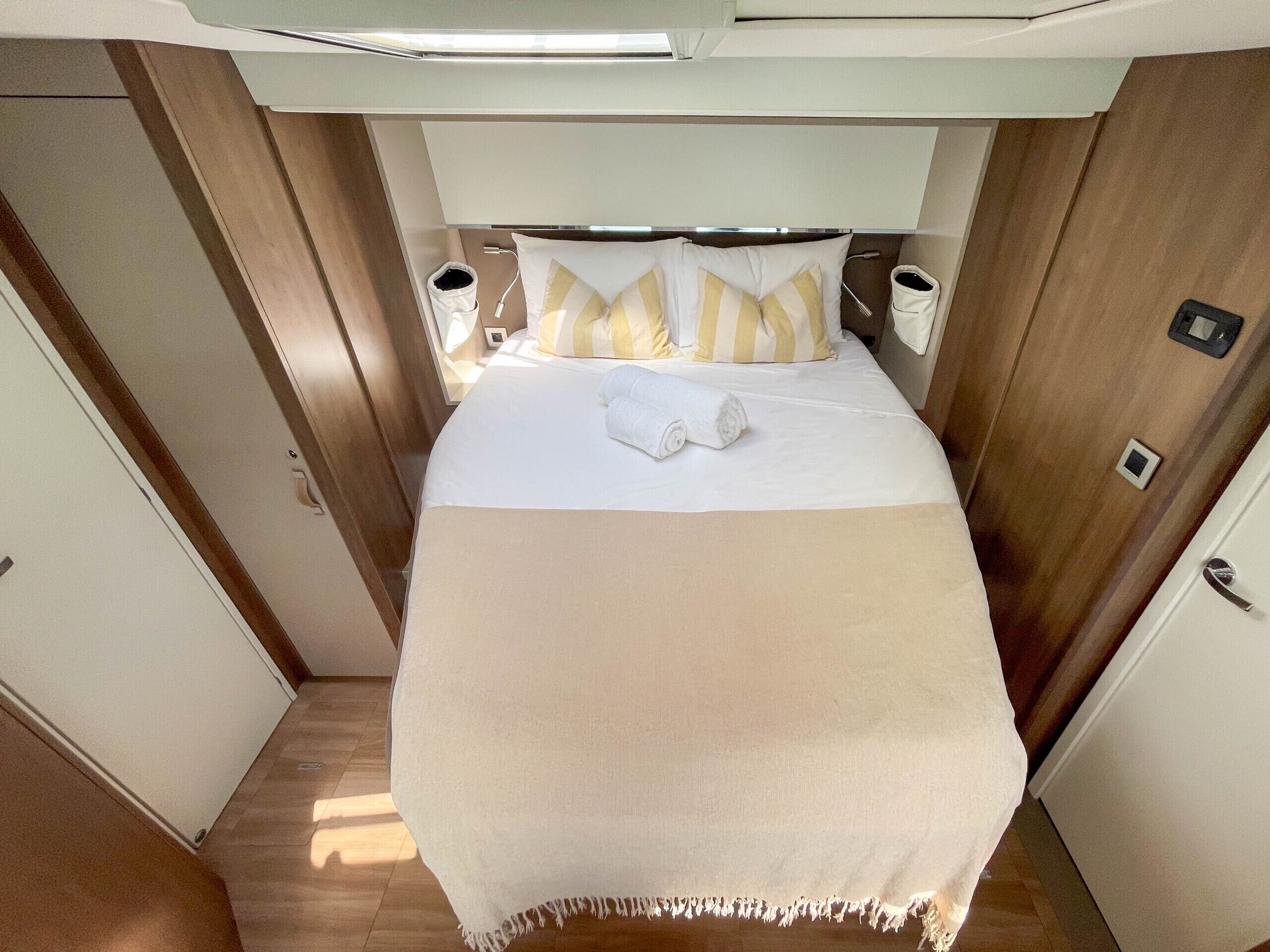 A compact bedroom with a bed, pillows, a blanket, bedside tables, and a door.