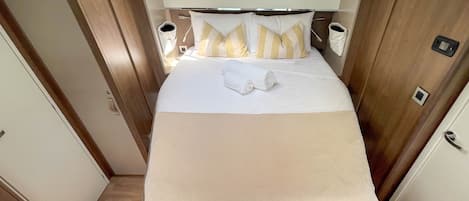 A compact bedroom with a bed, pillows, a blanket, bedside tables, and a door.