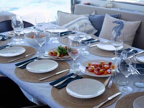 Ein Esszimmer mit gedecktem Tisch, Geschirr, Besteck und Gläsern, mit Blick auf das Meer im Hintergrund.