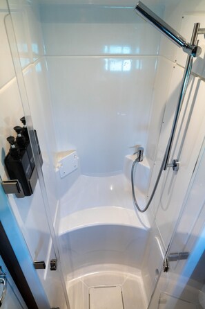 Une cabine de douche fermée par des parois en verre, dotée d’un pommeau de douche à main, d’un système de commande à main pour la douche et d’un robinet mural.