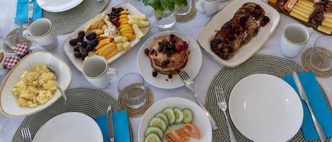 Aamiastarvikkeilla katettu pöytä, jossa on esimerkiksi pannukakkuja, juustoa ja hedelmiä.