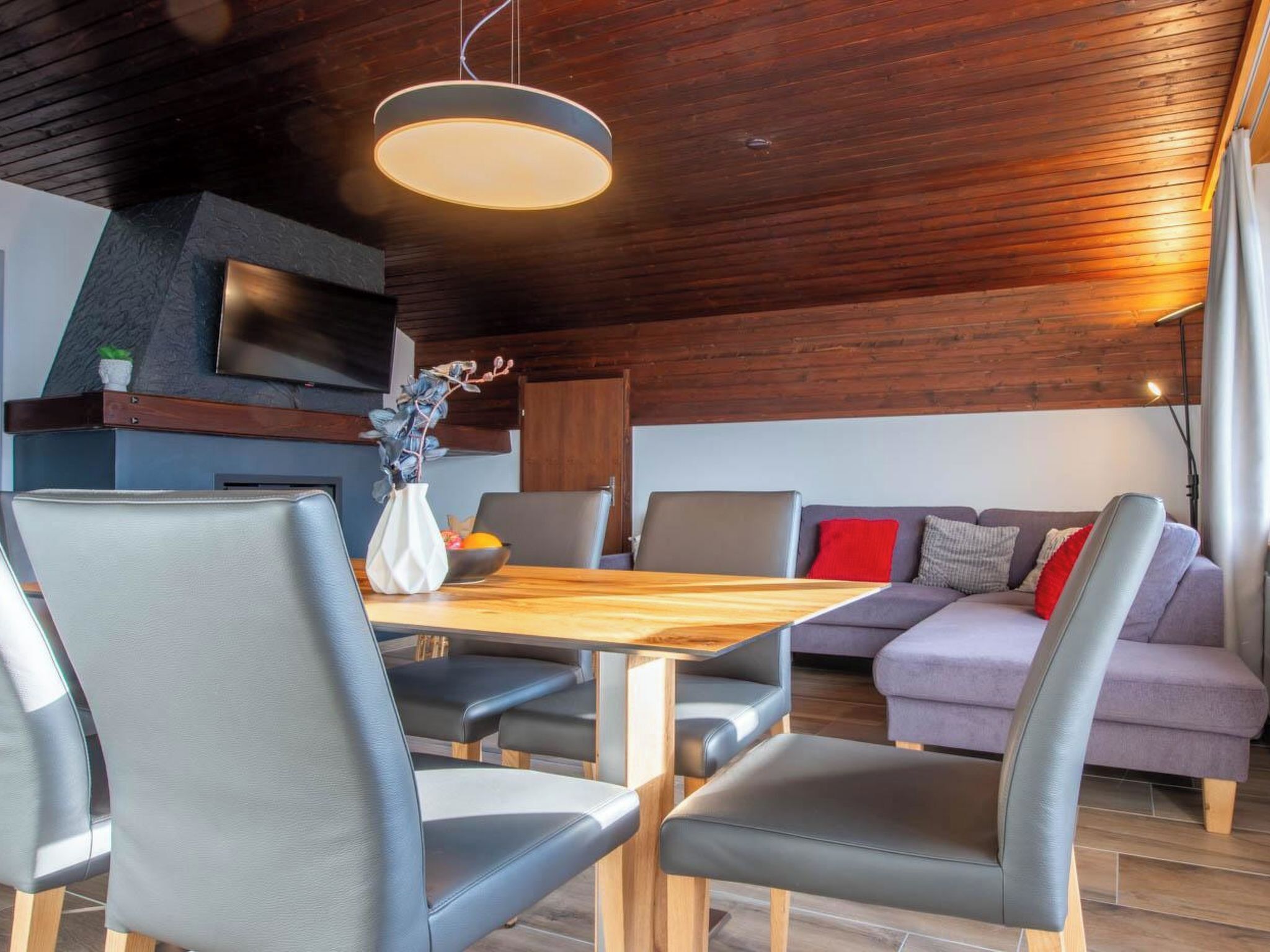 Un intérieur moderne avec un plafond en bois, un coin repas comprenant une table et des chaises, et un espace détente avec un canapé.