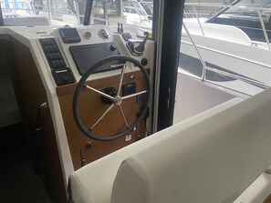 De bestuursruimte van een boot, met een stuurwiel, bedieningspaneel en zitgedeelte.