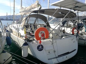 Un velero amarrado en un puerto deportivo, con boyas salvavidas y un logotipo que indica 'Perfect Sailing'.