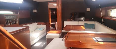 A boat interior with a sofa, a table, a television, and a cabinet with bottles.