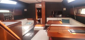 L'intérieur d'un bateau, avec un canapé, une table, un téléviseur et un meuble contenant des bouteilles.