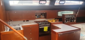 A compact kitchen with a stove, sink, and cabinets, and a small window above the sink. - Sun-Kissed Sailing Adventure in the Ionian Islands, Lefkada (Lefkada)