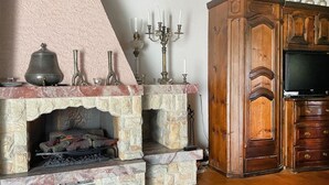Een stenen openhaard met een schoorsteenmantel, een televisie op een houten kast, en een kandelaar met kaarsen.