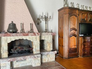 A stone fireplace with a mantel, a television on a wooden cabinet, and a candelabra with candles. - Fifinhaus 1. OG Süd Appartement/Fewo, Dusche und Bad, WC, 3 Schlafräume by Interhome (Fiesch)