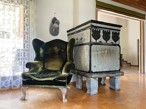 A room with a wooden floor, a dark upholstered chair, and a stone pedestal with decorative elements. - Fifinhaus 1. OG Süd Appartement/Fewo, Dusche und Bad, WC, 3 Schlafräume by Interhome (Fiesch)