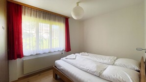 Een slaapkamer met een houten bed, een radiator, een raam met rode gordijnen en een witte plafondlamp.