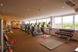 Een sportschool met cardioapparaten, gewichtbanken en dumbbells.