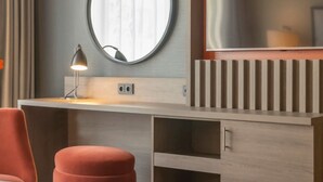 A modern room with a round mirror, a desk with a lamp, and a red chair.