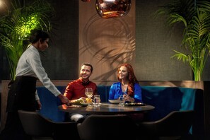 Een restaurant met een blauwe zithoek, een bediende die een maaltijd serveert en een decoratieve muur met een rond patroon.