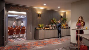 A hotel lobby with a reception desk, a Grand Canal Suite sign, a buffet with various food items, and a seating area with orange chairs.