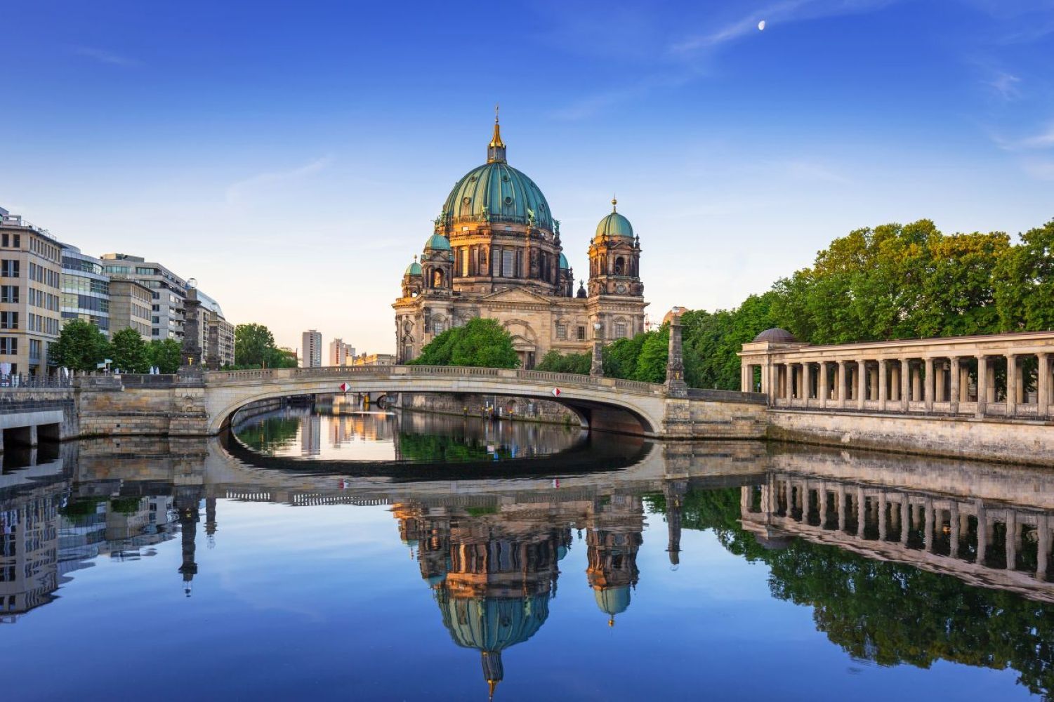 A historic building with a large dome and two smaller domes, reflecting in a calm body of water.