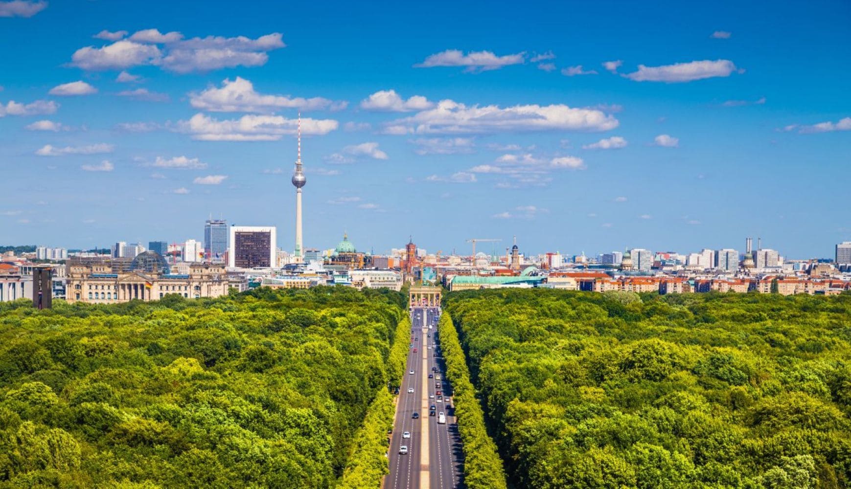A cityscape with a prominent tower, a road lined with trees, and a variety of buildings.