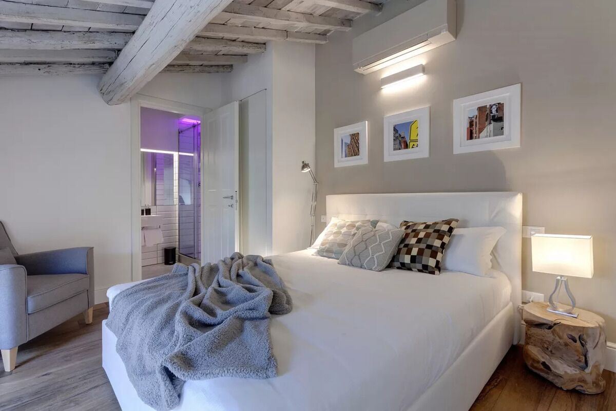 Un dormitorio con una cama grande, una lámpara de noche, una silla y una puerta que da a un baño.