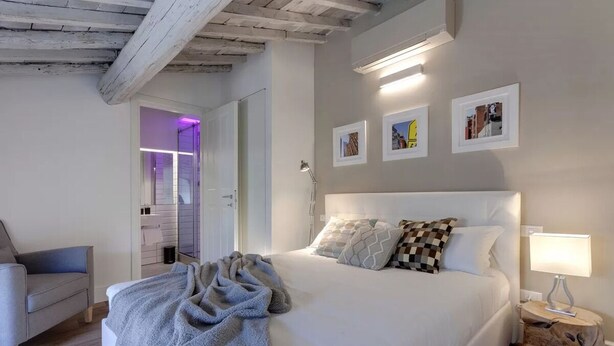 Un dormitorio con una cama grande, una lámpara de noche, una silla y una puerta que da a un baño.