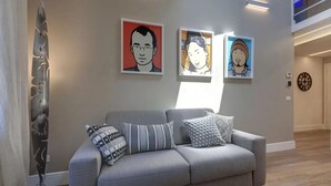Una sala de estar moderna con un sofá gris, tres cuadros enmarcados en la pared y una lámpara de pie alta.