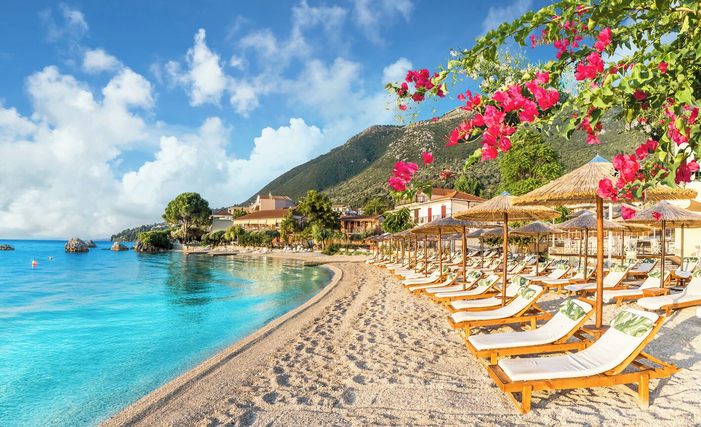A beach with clear blue water, a sandy shore, and wooden lounge chairs under umbrellas.