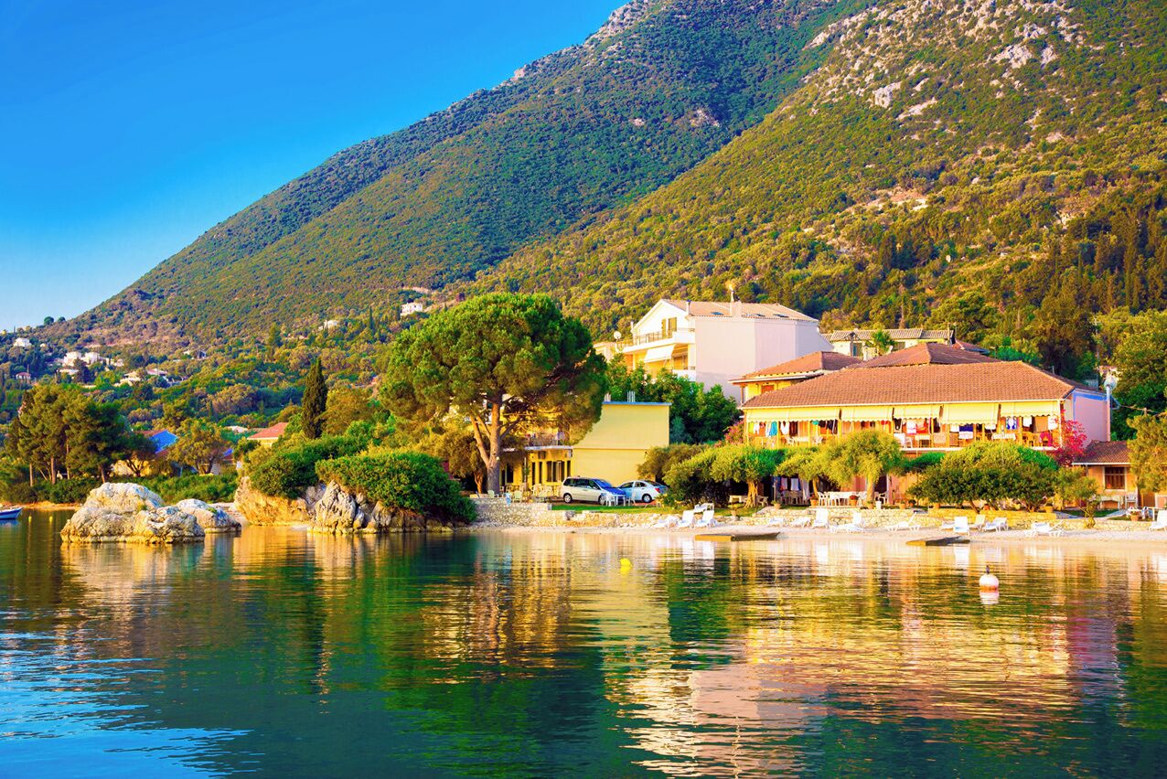 Un hotel frente al mar con montañas al fondo, una playa y un lago tranquilo.