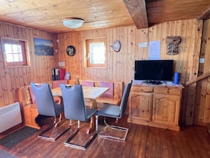 Een houten interieur met een eettafel, stoelen, een televisie en een klok aan de muur.