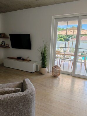 A living room with a flat-screen TV, a potted plant, a wicker chair, and a sliding glass door leading to an outdoor patio. - Villa Sunrise Labin, Istria - a smile every day (Nedešćina)