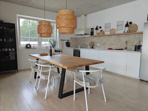Une cuisine moderne avec une table à manger en bois, des chaises blanches, des suspensions en osier et un pare-feu en pierre.