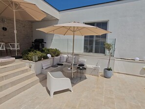 Un espace extérieur lumineux, aménagé avec un canapé, des chaises, une table et un grand parasol.
