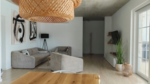 Ein modernes Wohnzimmer mit Couchtisch aus Holz, grauem Ecksofa, einer schwarzen Stehlampe und einem großen Fenster.