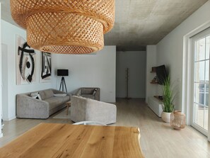 Ein modernes Wohnzimmer mit Couchtisch aus Holz, grauem Ecksofa, einer schwarzen Stehlampe und einem großen Fenster.