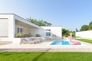 Ein modernes Haus mit Schwimmbad, Sitzgelegenheiten im Freien und einem rosa Flamingo-Schwimmpfad.