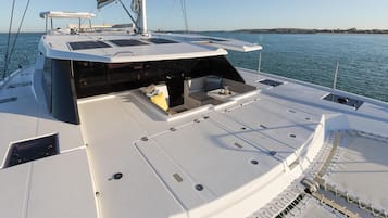 Het dek van een boot met zitplaatsen, een mast en uitzicht op het water.