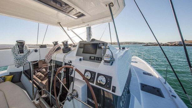 A yacht's deck with a steering wheel, control panel, and seating area.