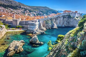 A coastal town with a historic stone bridge, clear turquoise waters, and a mountainous backdrop.