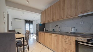 A modern kitchen with wooden cabinets, a built-in oven, and a dining area with a table and chairs. - V & G Apartment by Rentals Pro - Nea Moudania (Nea Moudania)